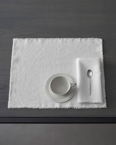 a white place mat with a cup and saucer on it next to a spoon