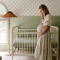 a pregnant woman standing next to a crib in a room with green walls and floral wallpaper