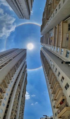 the view from below looking up at tall buildings and a rainbow in the blue sky