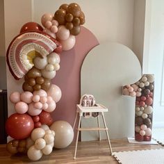 balloons are arranged in the shape of an arch on a wall next to a chair