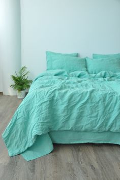 a bed with green sheets and pillows in a white room next to a potted plant