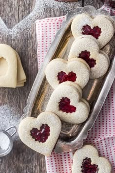 heart shaped cookies with jam in the middle on a table next to other desserts