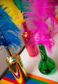 two colorful vases filled with feathers on top of a table