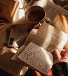 someone is holding an open book with writing on it in front of some books and coffee mugs