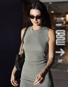 a woman in grey dress and sunglasses walking down the street