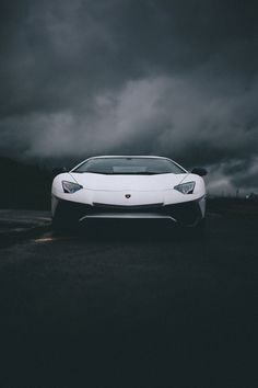 a white sports car parked on the side of a road with dark clouds in the background