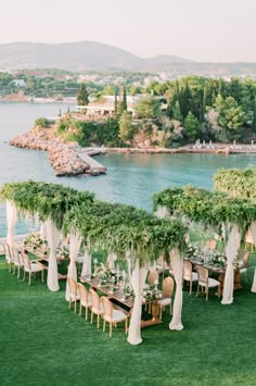 an outdoor dining area with tables and chairs covered in greenery next to the water