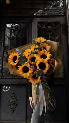 a woman holding a bouquet of sunflowers in front of a door