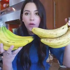 a woman holding two bunches of bananas in front of her face and looking at the camera