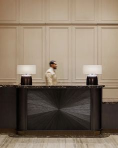 a man walking past a reception desk with two lamps