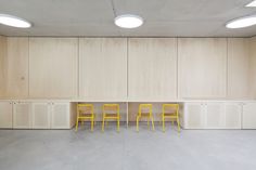 three yellow chairs are sitting in the middle of a room with white walls and cupboards