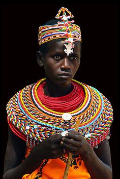 an african woman wearing colorful jewelry and holding a stick