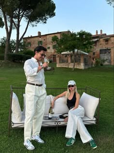 a man and woman sitting on top of a white couch in the middle of a field