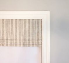 an open window with a white frame and striped roman blind on the top, in front of a gray wall