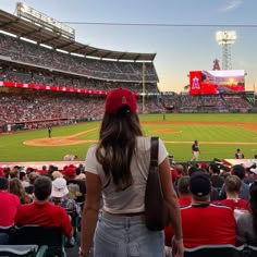 a woman standing on top of a baseball field next to a stadium filled with people