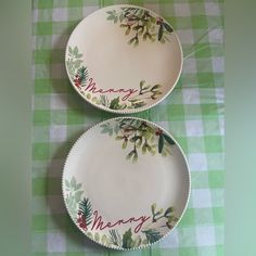 two plates with merry designs on them sitting on a green and white checkered tablecloth