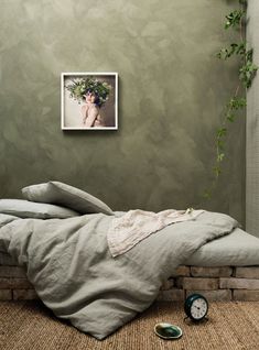 an unmade bed sitting in front of a green wall with a clock on the floor