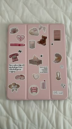 a pink tray with various stickers on it sitting on top of a white bed