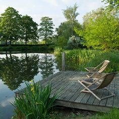 a lawn chair sitting on top of a wooden dock next to a lake and trees