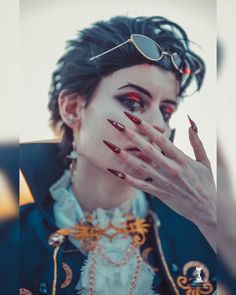 a woman with dark makeup and red nail polish holding her hand up to her face