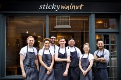 six people in aprons stand outside the front of sticky walnut