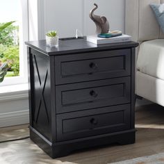 a black night stand with three drawers and a plant on the top, in front of a window