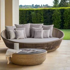 a wicker couch sitting on top of a wooden floor next to a table with pillows