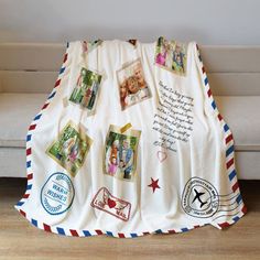 a white blanket with pictures and stamps on it is sitting on a couch next to a pillow