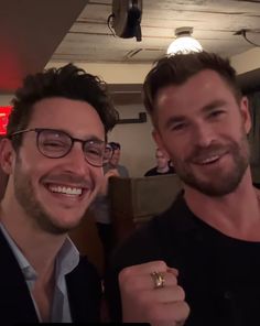 two men smiling at the camera with one holding a ring in front of his face