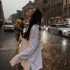 a woman with dreadlocks walking down the street in the rain while another man rides his bike behind her