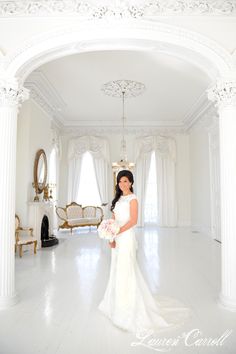 a woman in a white wedding dress standing in a room with columns and chandeliers