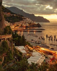 boats are docked in the water at dusk near a city on the shore and mountains