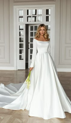 a woman in a white wedding dress standing on a wooden floor holding a flower bouquet