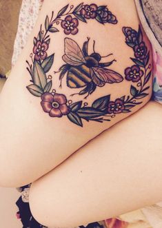 a woman's thigh with a bee and flowers tattoo on it