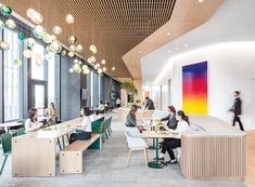 people are sitting at tables in an office setting with large windows and colorful artwork on the wall