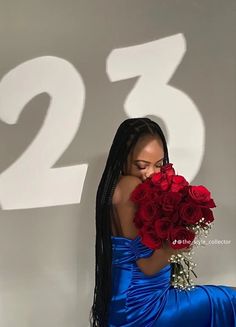 a woman in a blue dress holding a bouquet of red roses with the number twenty two behind her