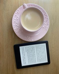 a tablet sitting next to a cup of coffee on top of a wooden table with a pink saucer