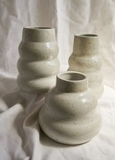 two white vases sitting on top of a white cloth covered tablecloth, one with black speckles and the other without