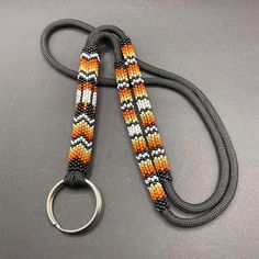 an orange, white and black beaded lanyard with a metal ring on a gray surface