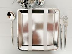 a silver tray with forks, spoons and mirror balls on it next to two disco ball decorations