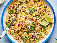 a bowl filled with corn and topped with cilantro, red onion, lime wedges