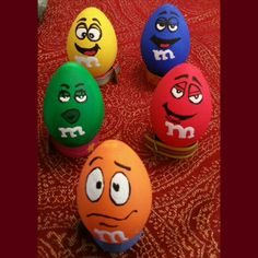 four eggs with faces painted on them sitting on a red tableclothed surface, one has