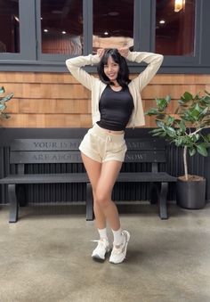 a woman posing in front of a bench with her hands on her head and wearing white shoes