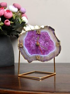 a purple clock sitting on top of a wooden table next to a vase with flowers