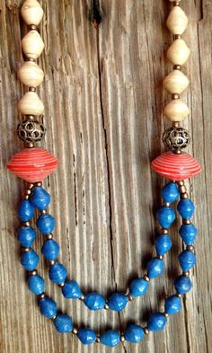 a blue and red beaded necklace on a wooden surface with beads hanging from it