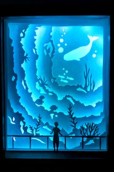 a person standing in front of a window with an underwater scene on the wall behind them