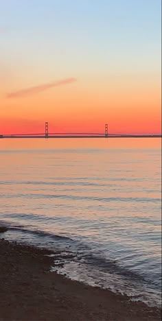 the sun is setting over the ocean with a bridge in the background