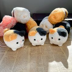 four small knitted cats sitting on top of a newspaper with yarn balls in the background