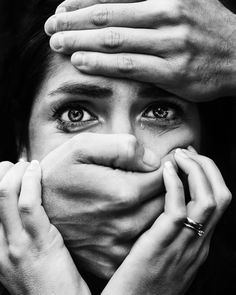 a woman covering her face with hands while looking at the camera, in black and white