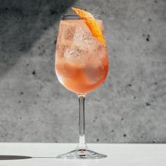 an orange garnish in a wine glass on a white countertop with concrete wall behind it